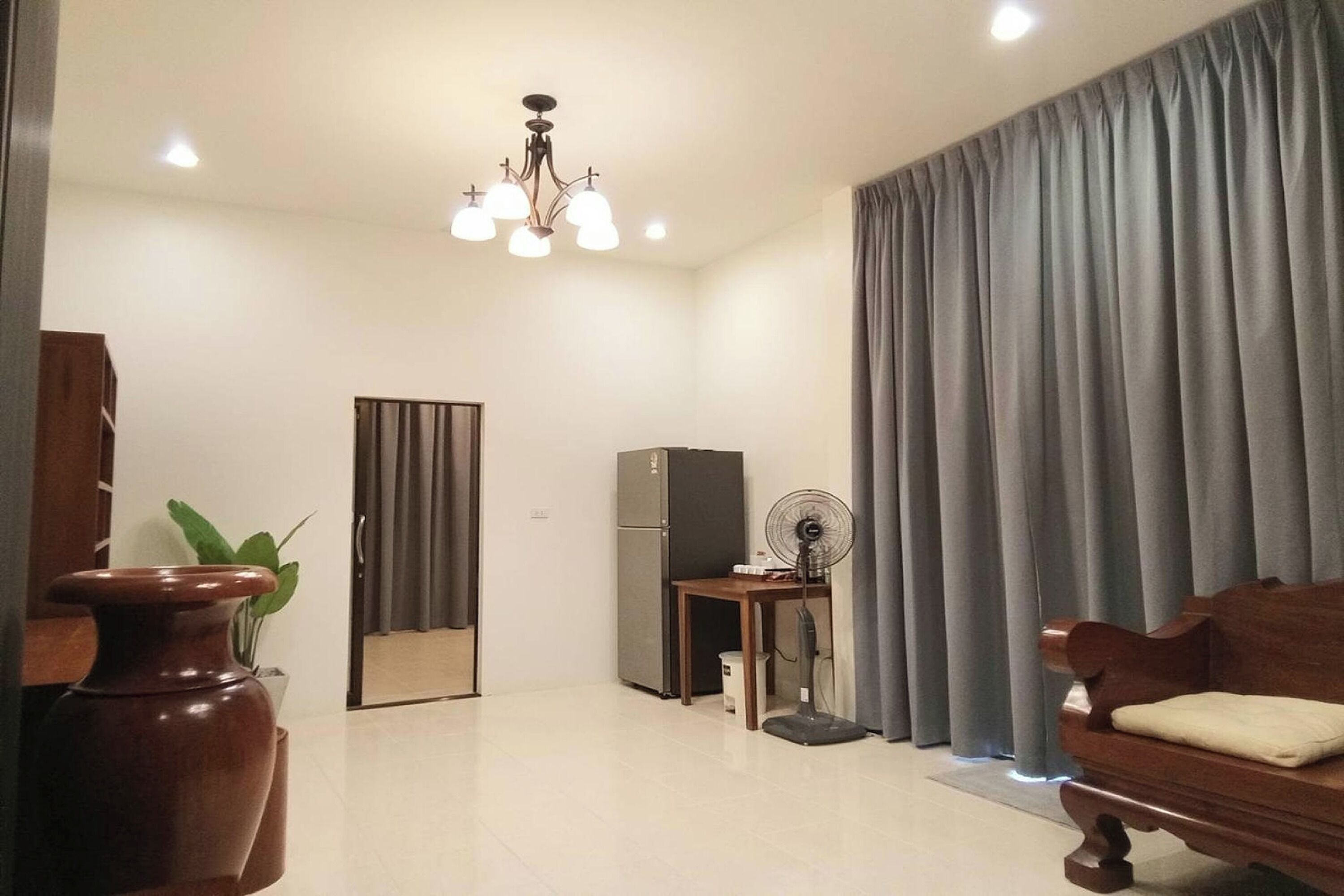 Una sala de estar con un sofá de madera, una mesa con un ventilador, un refrigerador y un florero con una planta.