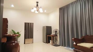 Una sala de estar con un sofá de madera, una mesa con un ventilador, un refrigerador y un florero con una planta.