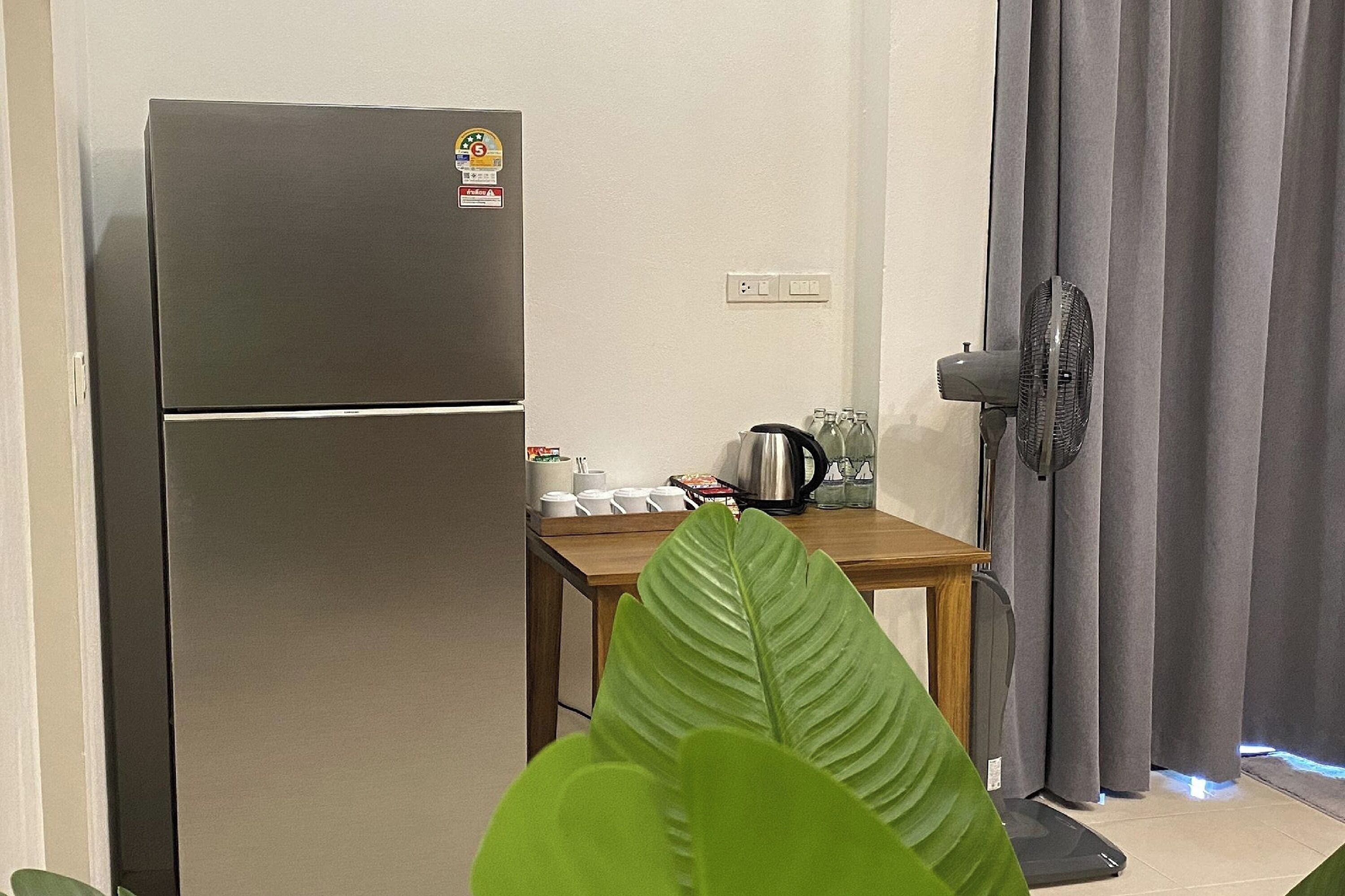 Une cuisine compacte équipée d’un réfrigérateur, d’une petite table avec ustensiles de cuisine et d’un ventilateur.