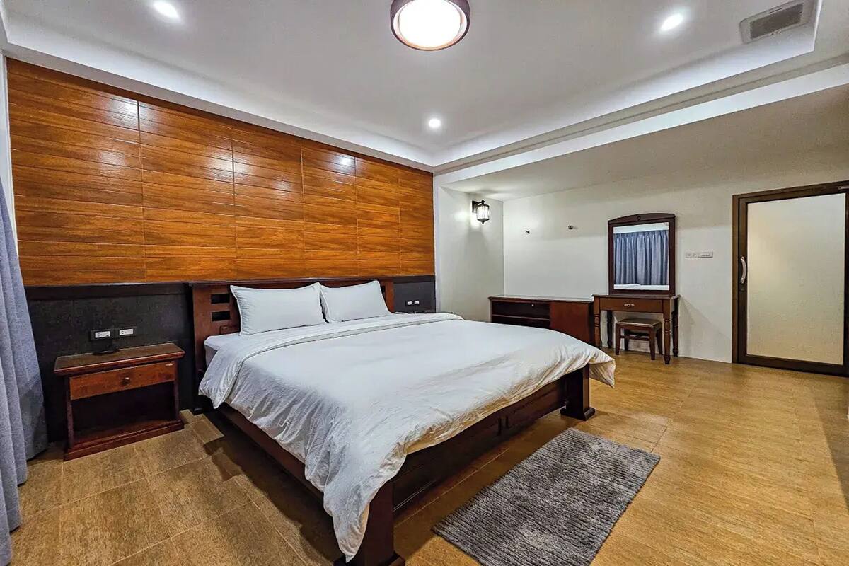 A modern bedroom with a wooden headboard, a large bed, bedside tables, a desk, and a mirror.