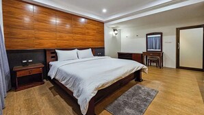 A modern bedroom with a wooden headboard, a large bed, bedside tables, a desk, and a mirror.