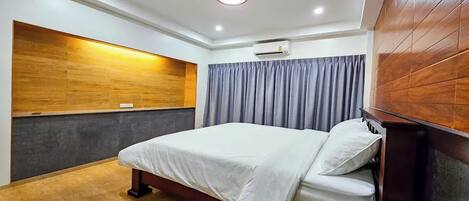 A modern hotel room with a large bed, wooden panel wall, grey curtains, and a ceiling light.