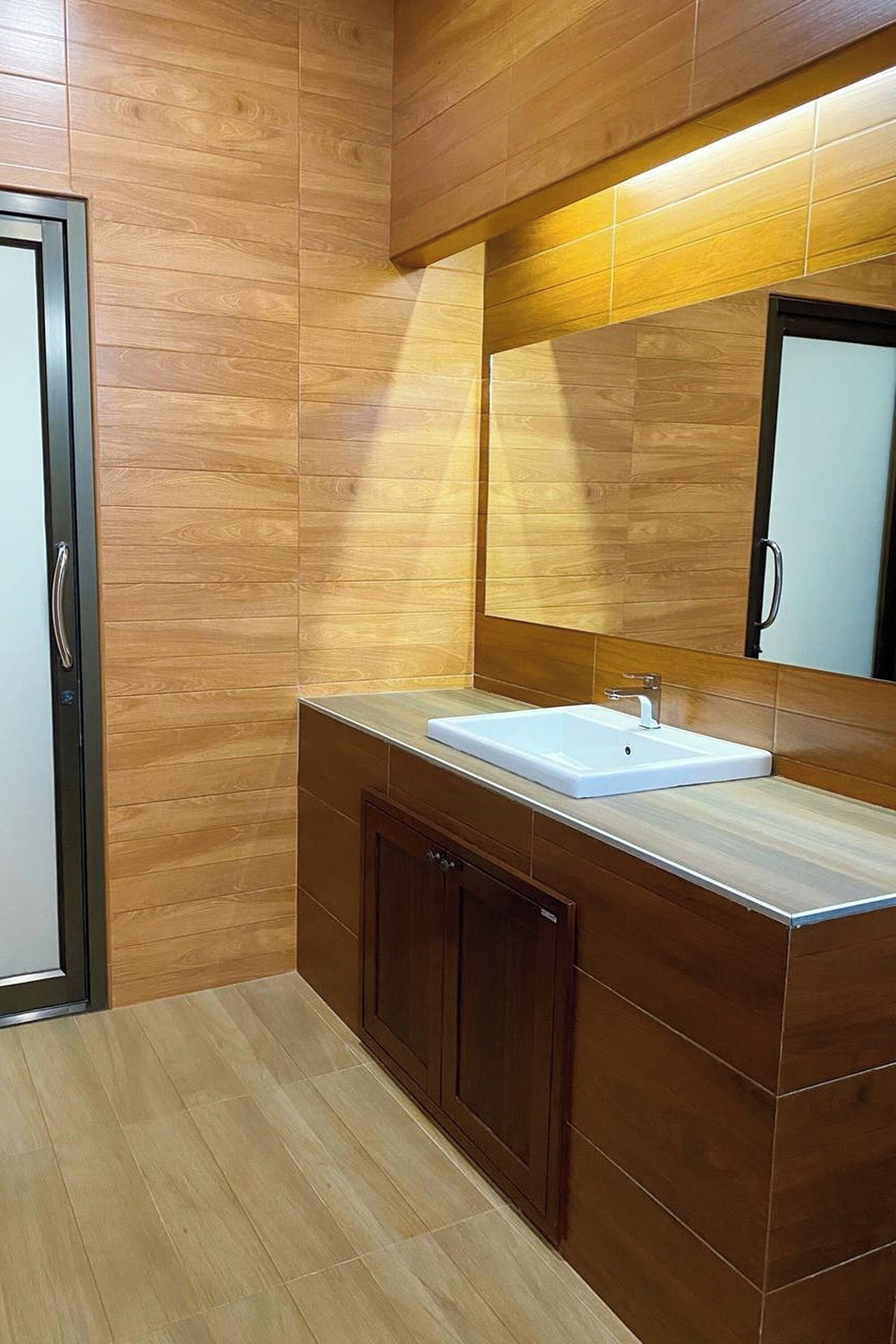Un baño moderno con paneles de madera, un lavamanos blanco y un espejo grande.