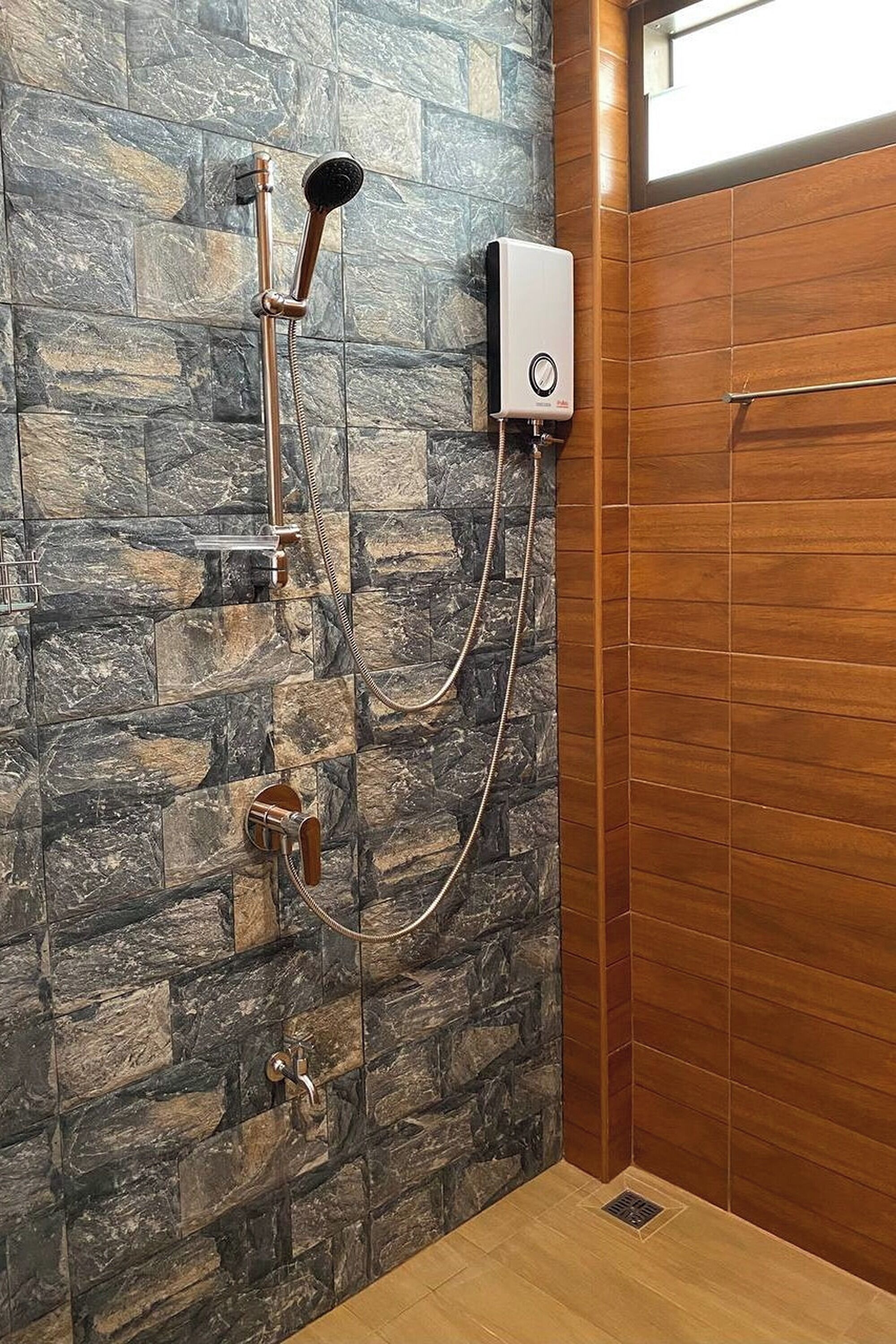 Una ducha con pared de piedra, pared de paneles de madera y unidad de control.