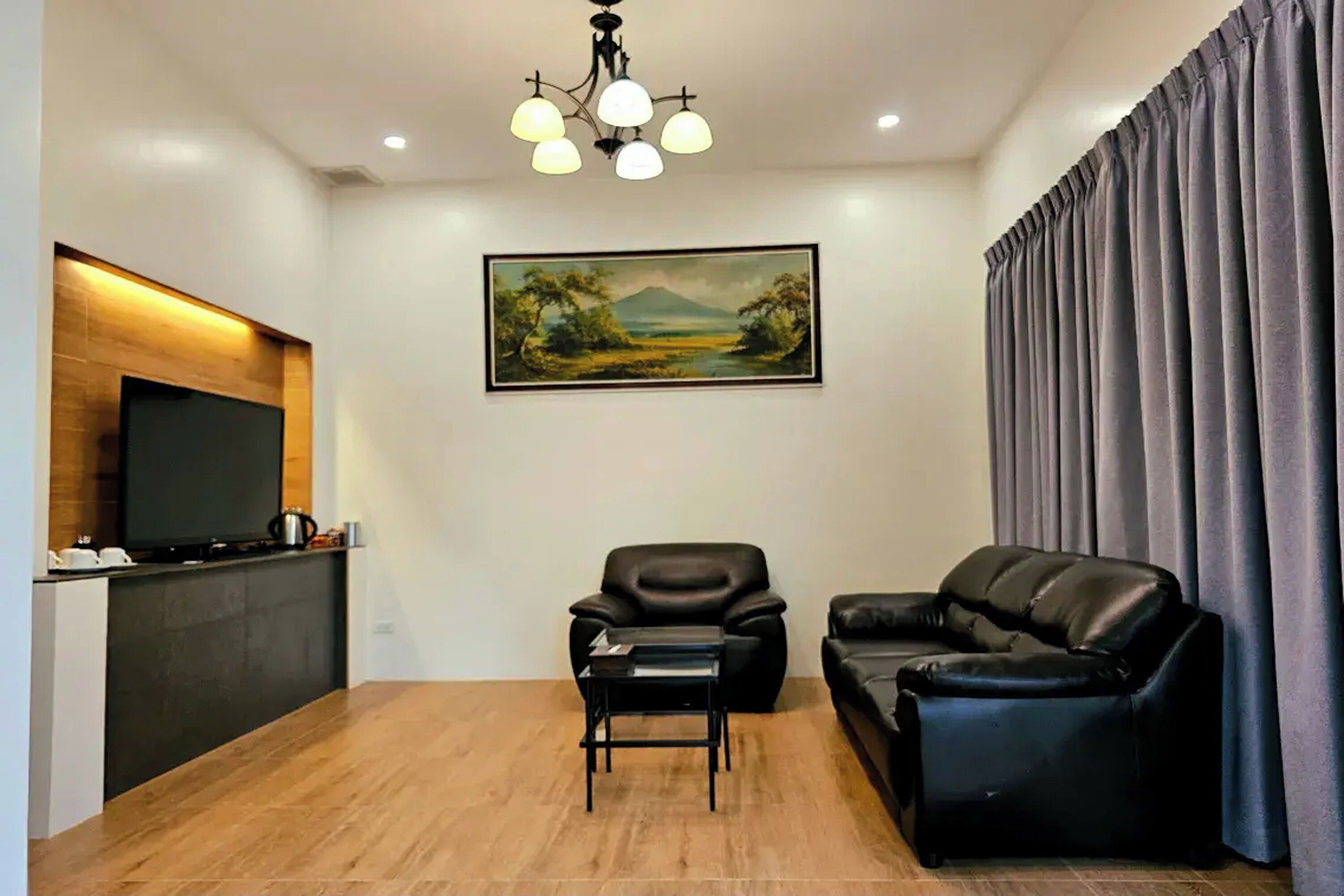 Een woonkamer met een flatscreen televisie, een schilderij, een bank, een stoel en een salontafel.