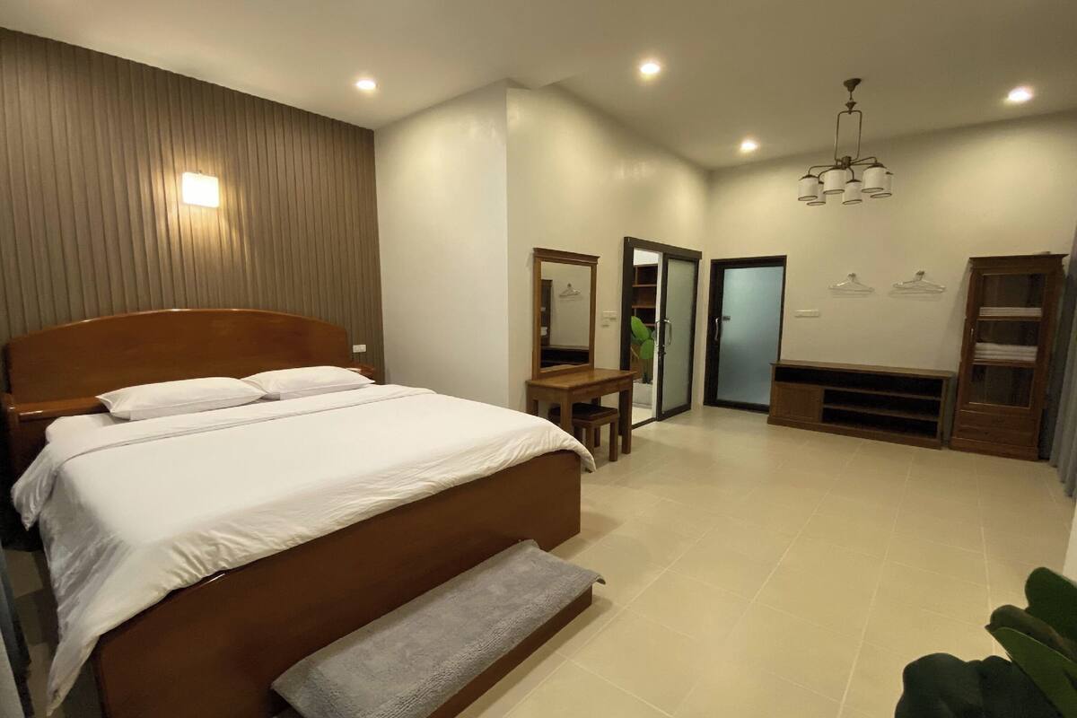 A modern bedroom with a wooden bed, a bench, a desk, and a mirror.