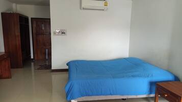 A bedroom with a bed, a wooden wardrobe, a door, and an air conditioning unit on the wall.