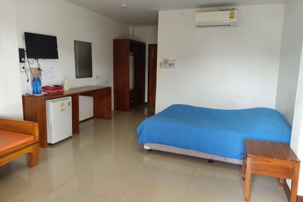 A room with a bed, a desk, a small refrigerator, a television, and an air conditioning unit.