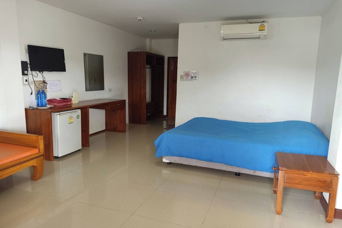 Una habitación de hotel con cama, escritorio, silla, refrigerador pequeño, televisor montado en la pared y aire acondicionado.