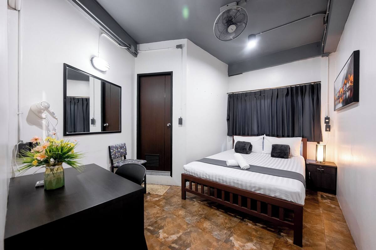 Une chambre d’hôtel comprenant un lit, une table de chevet, une chaise, un bureau et un vase de fleurs.