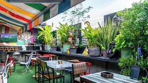 Un espace extérieur aménagé avec des tables et des chaises, entouré de plantes en pot et orné d’une fresque murale.