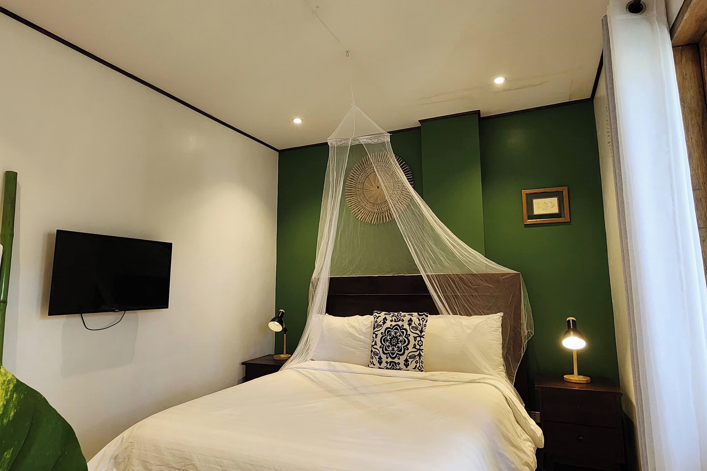 A neatly made bed with a canopy, a bedside lamp, and a wall-mounted TV.