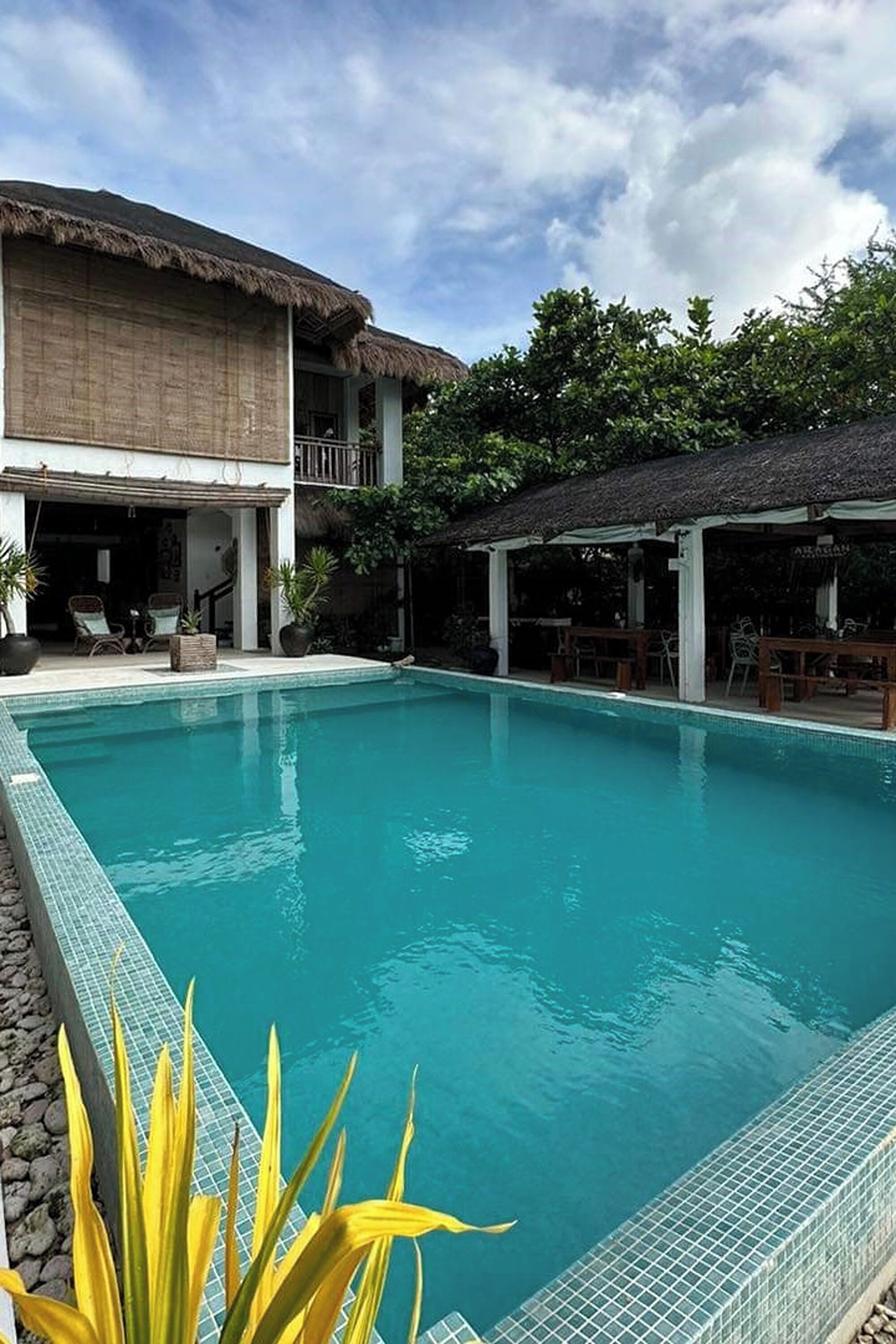 A swimming pool with a tiled edge, surrounded by lounge chairs and a covered seating area.