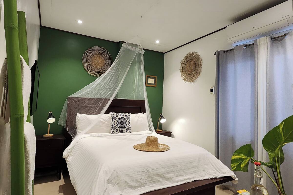 A neatly made bed with a canopy, a bedside lamp, and a decorative hat on the pillow.