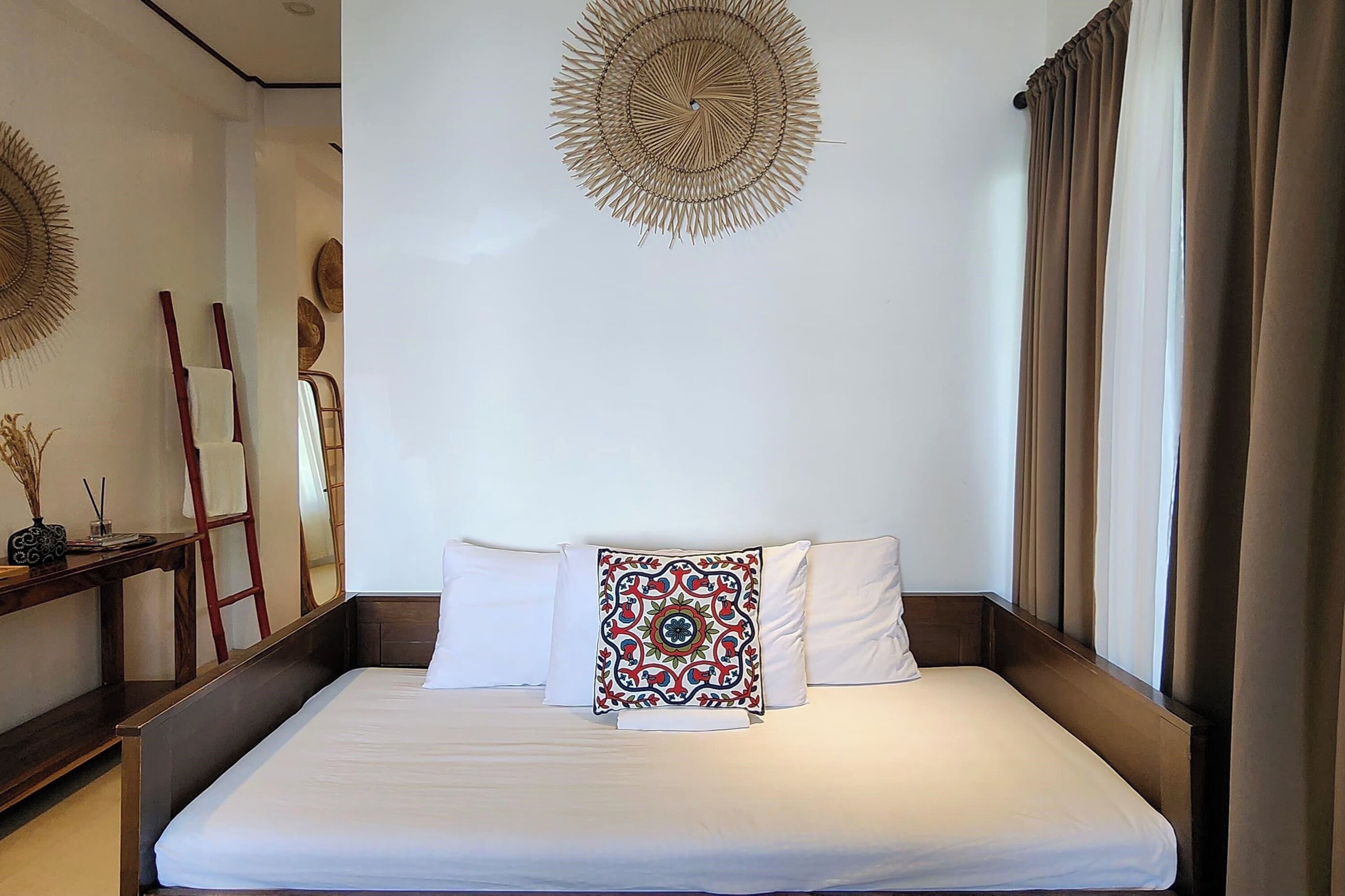A neatly made bed with white linens, a decorative pillow, and a wall hanging above it.