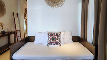 A neatly made bed with white linens, a decorative pillow, and a wall hanging above it.