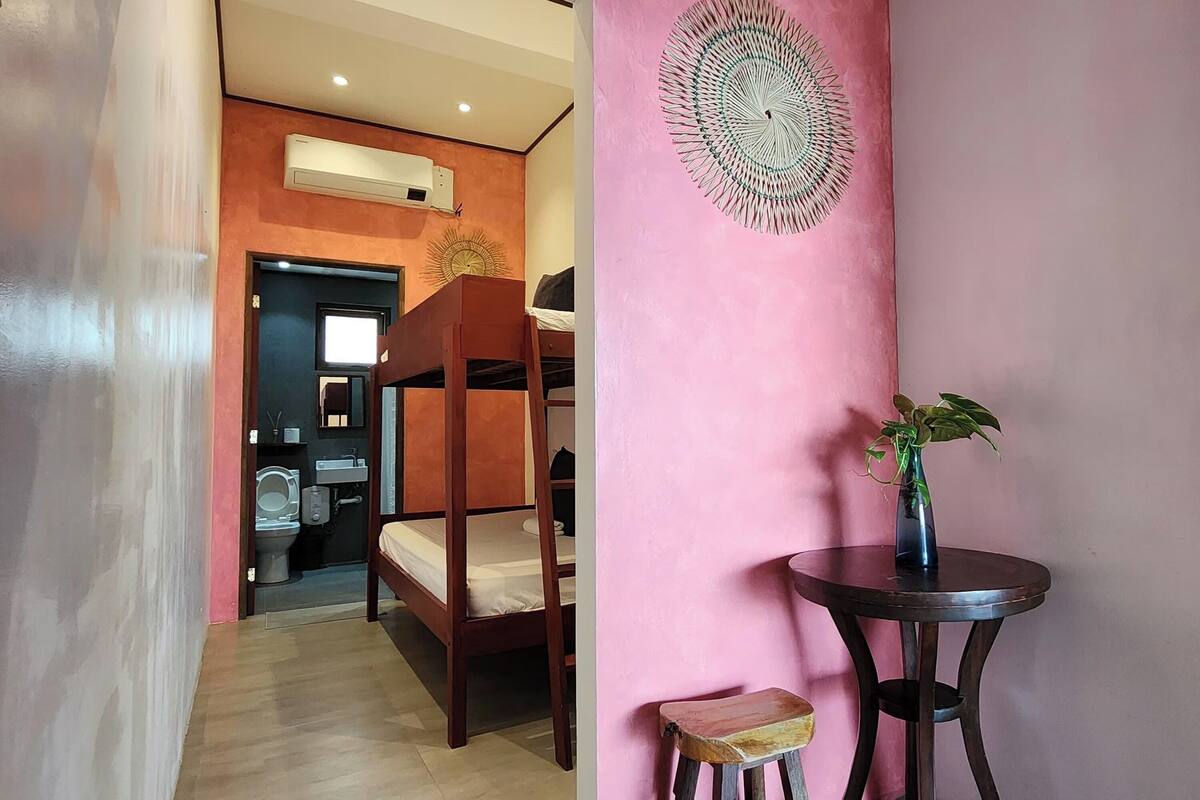 A room with a bunk bed, a small table with a plant, and a decorative wall piece.