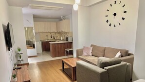Moderni olohuone, jossa on sohva, sohvapöytä, televisio ja taustalla näkyy keittiö.