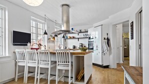 Una cocina moderna con armarios blancos, una isla central con sillas, una estufa grande y un televisor montado sobre la isla.