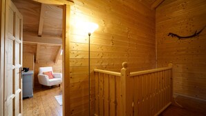 Un intérieur en bois avec une chaise blanche et une petite table, une rambarde en bois et un luminaire.