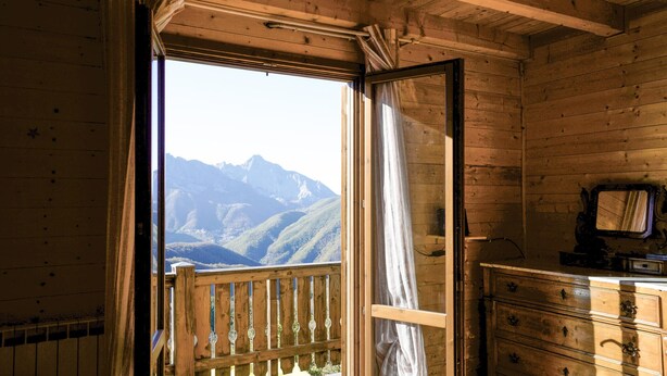 Une pièce de cabane en bois avec une grande fenêtre, des poutres en bois au plafond, une commode en bois et un miroir.