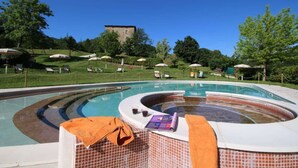 A hot tub with a tiled interior, surrounded by a pool, and a view of a hill with a building in the background. - Apartment in Marche near Urbino and Pool (Apecchio)