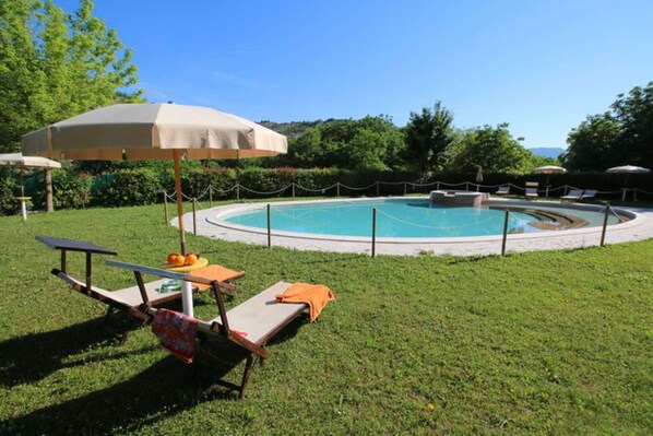 A swimming pool with lounge chairs and a picnic table, surrounded by a fence and greenery. - Apartment in Marche near Urbino and Pool (Apecchio)