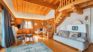 A cozy living room with wooden beams, a staircase, a sofa, and a coffee table. - Chalet in Kitzbühel near Ski Lifts (Kitzbühel)