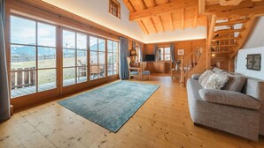 A spacious living area with large windows, a wooden staircase, and a cozy sofa. - Chalet in Kitzbühel near Ski Lifts (Kitzbühel)