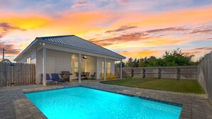 Ein Schwimmbad mit überdachter Terrasse, einem Holzzaun und einem Sonnenuntergangshimmel.