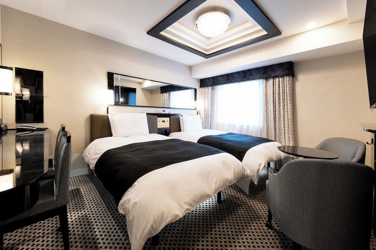A hotel room with two beds, a desk, a chair, a mirror, and a ceiling light fixture.