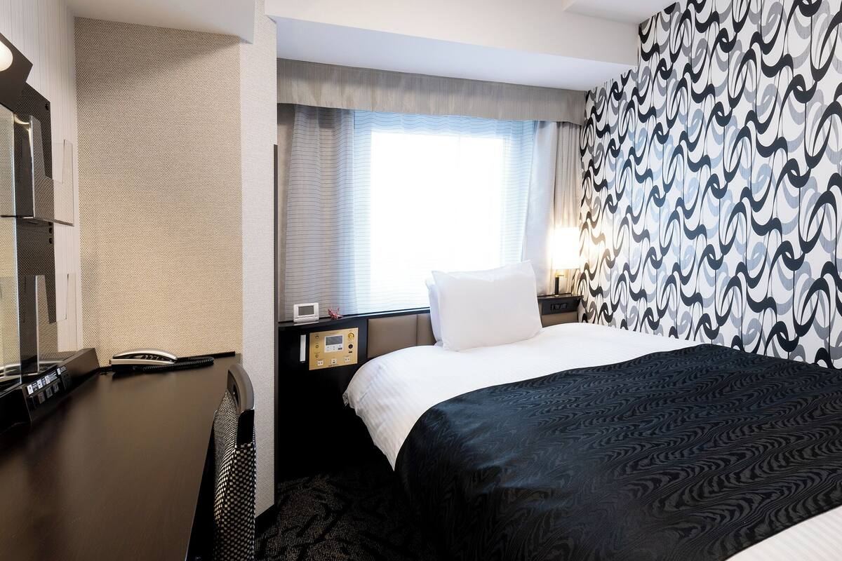 A hotel room with a bed, bedside table, lamp, and a patterned wall.