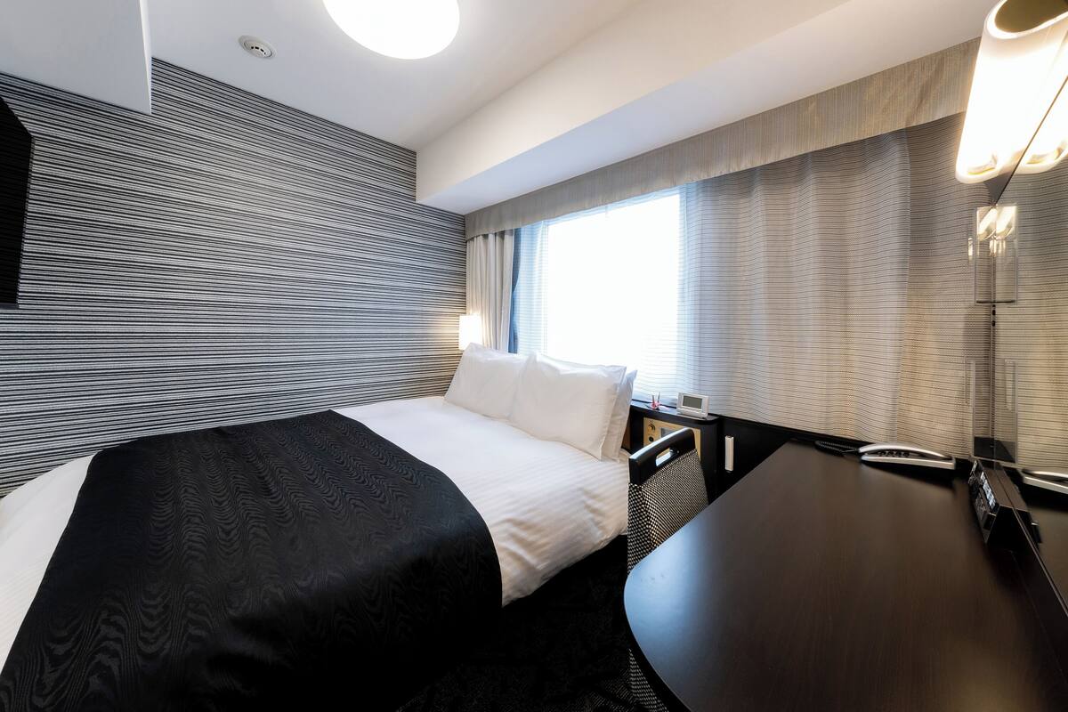 A modern hotel room with a large bed, a desk, and a window with curtains.
