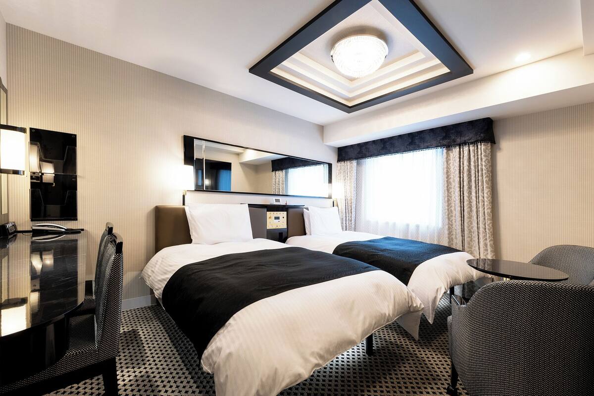 A hotel room with a bed, a desk, a chair, a TV, and a ceiling light.