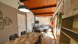 A dining area with a wooden table, chairs, and a decorative wall. There is a door, a television, and a sofa in the background.