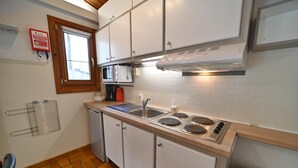 A kitchen with white cabinets, a microwave, a stove, and a window with blinds.