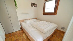 A bedroom with a bed, a wardrobe, a window, and a wall-mounted shelf.