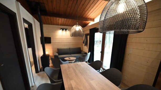 Een modern interieur met een houten eettafel, zwarte stoelen, een bank en een hanglamp.