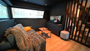 A modern living room with a sofa, a small table, a television, and a staircase.