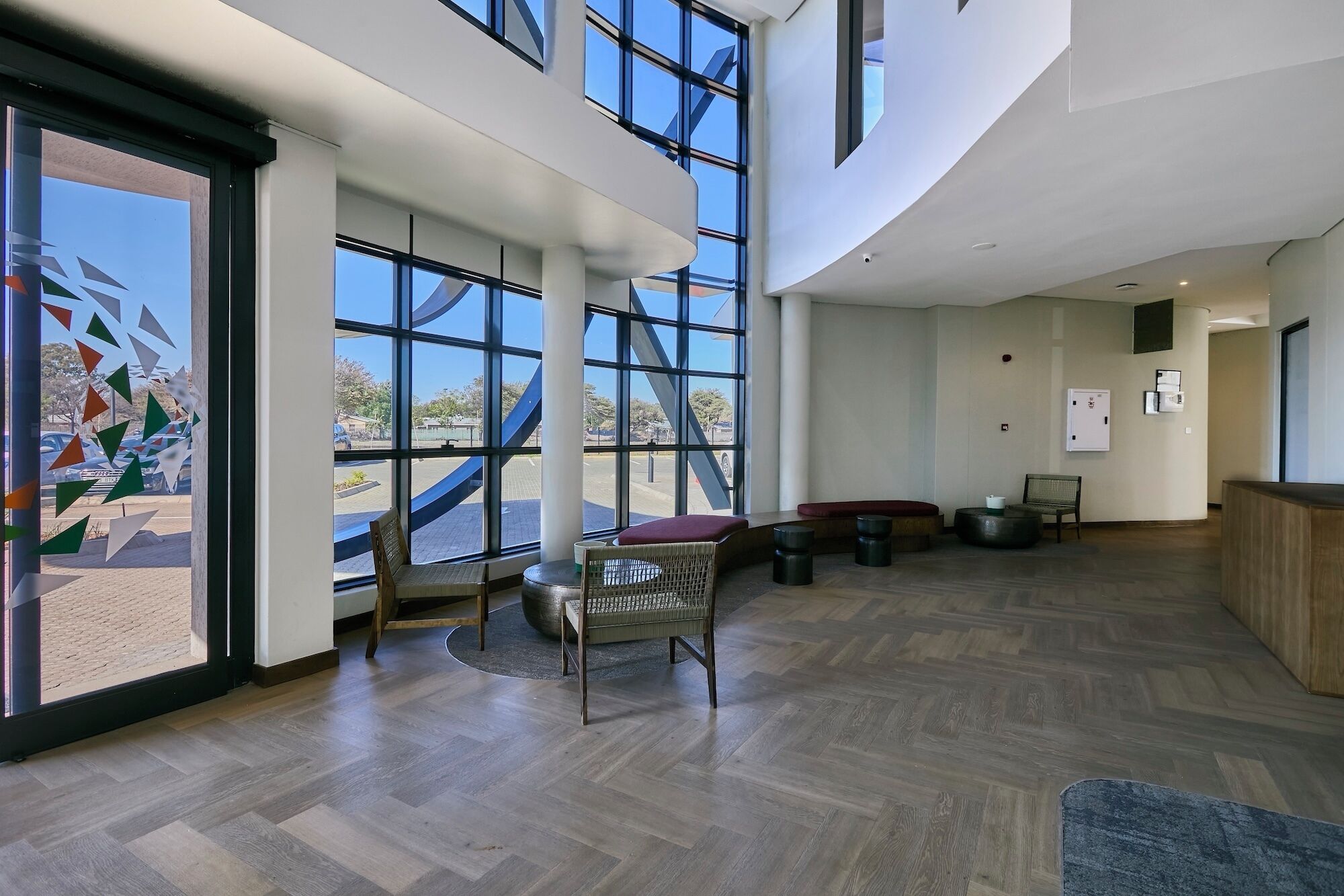 Un lobby amplio con ventanas grandes, piso de madera y un área de descanso con banca y sillas.