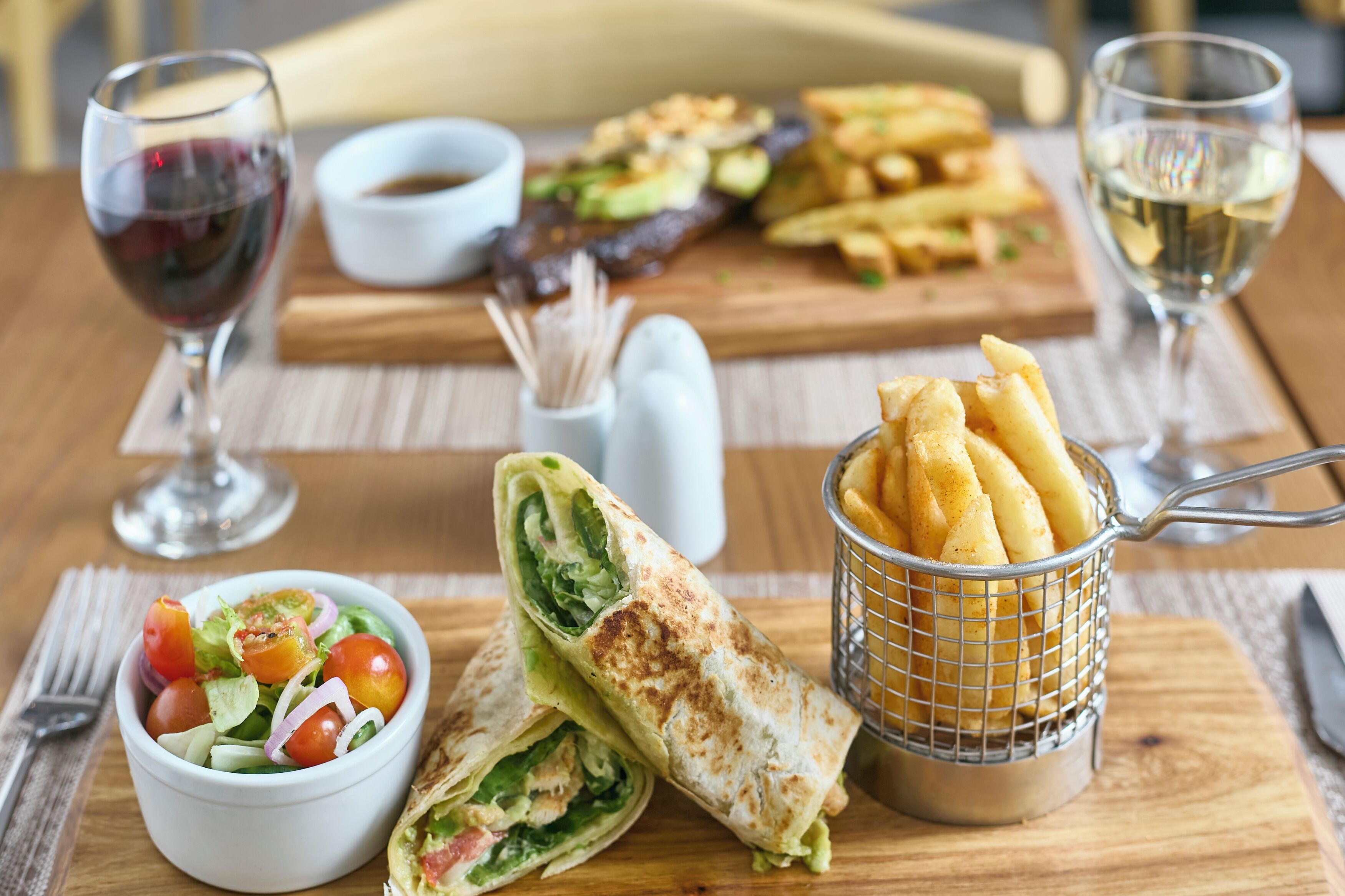 A table with a salad, a wrap, fries, and two glasses of wine.