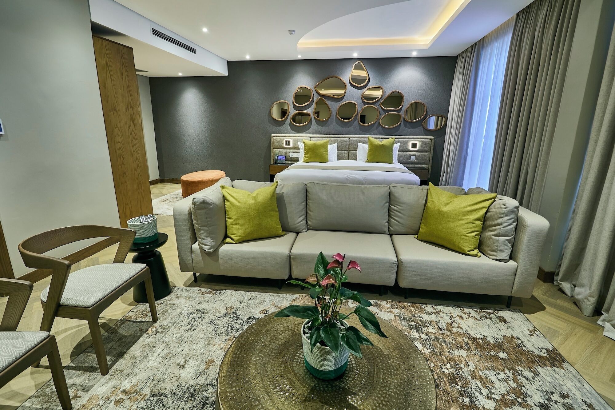 A modern hotel room with a sofa, a coffee table with a plant, and a bed with a headboard.