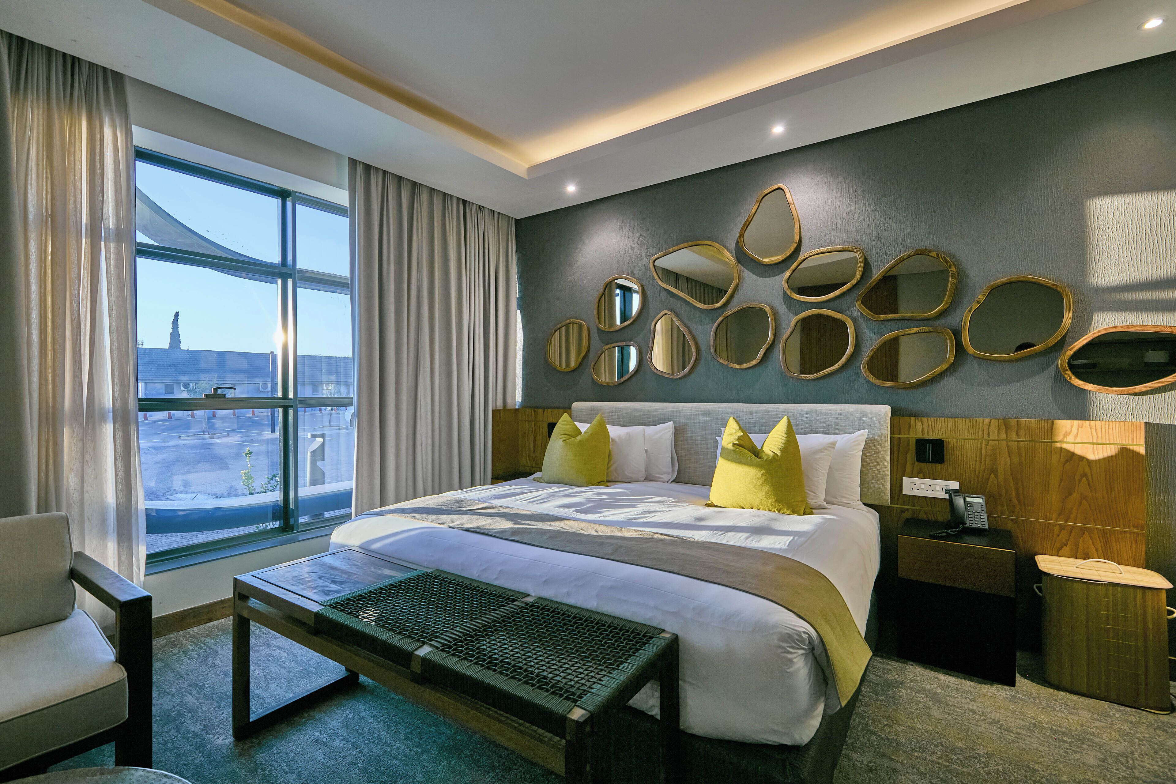 Una habitación de hotel con una cama grande, una mesita de noche, una silla, una ventana con cortinas y una pared con espejos decorativos.