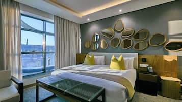 Una habitación de hotel con una cama grande, una mesita de noche, una silla, una ventana con cortinas y una pared con espejos decorativos.