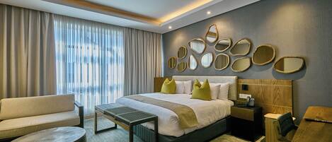 A modern hotel room with a large bed, a sofa, a round table, and a desk.