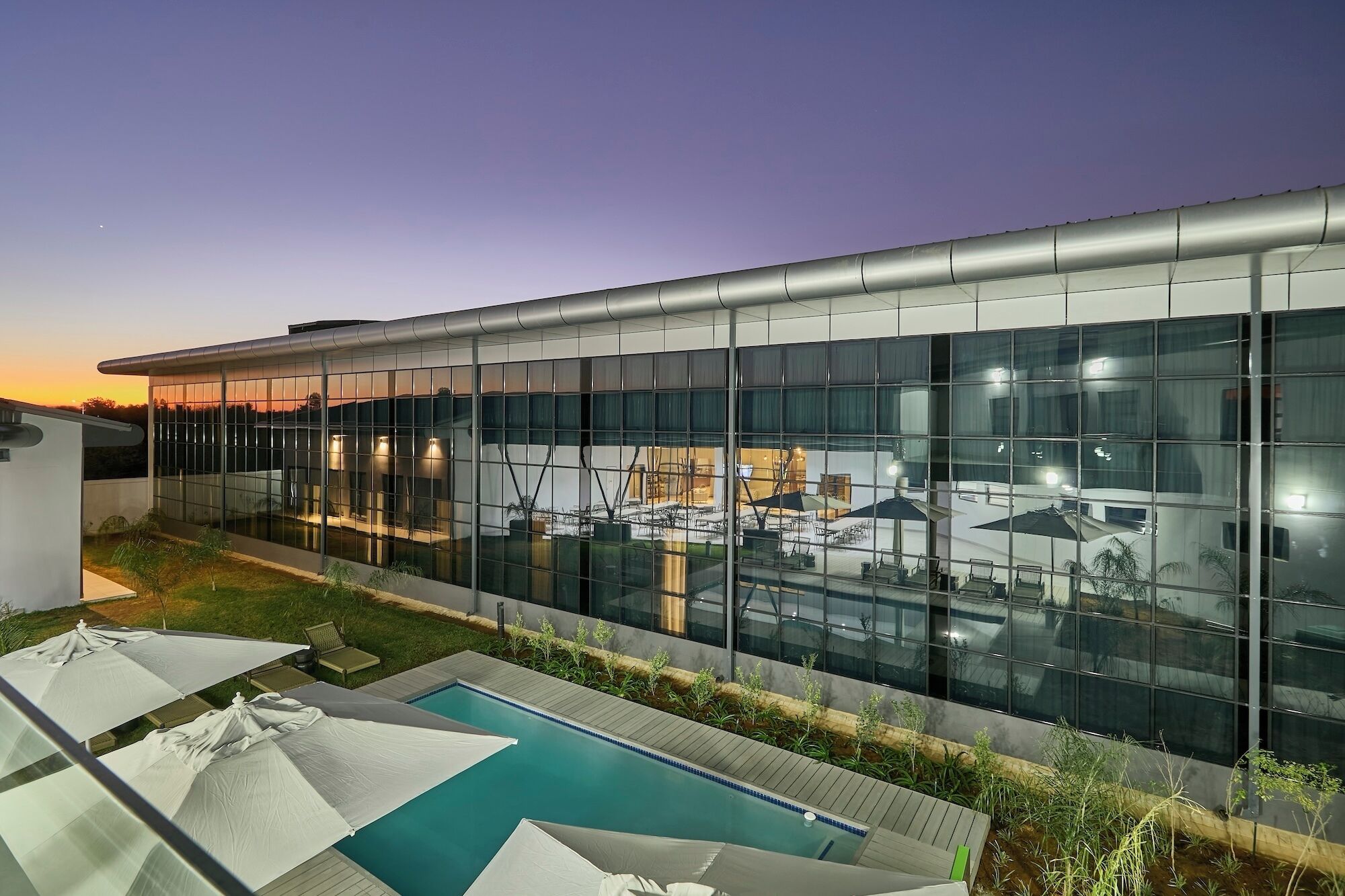 Un edificio moderno con fachada de vidrio, piscina y mobiliario para exteriores.