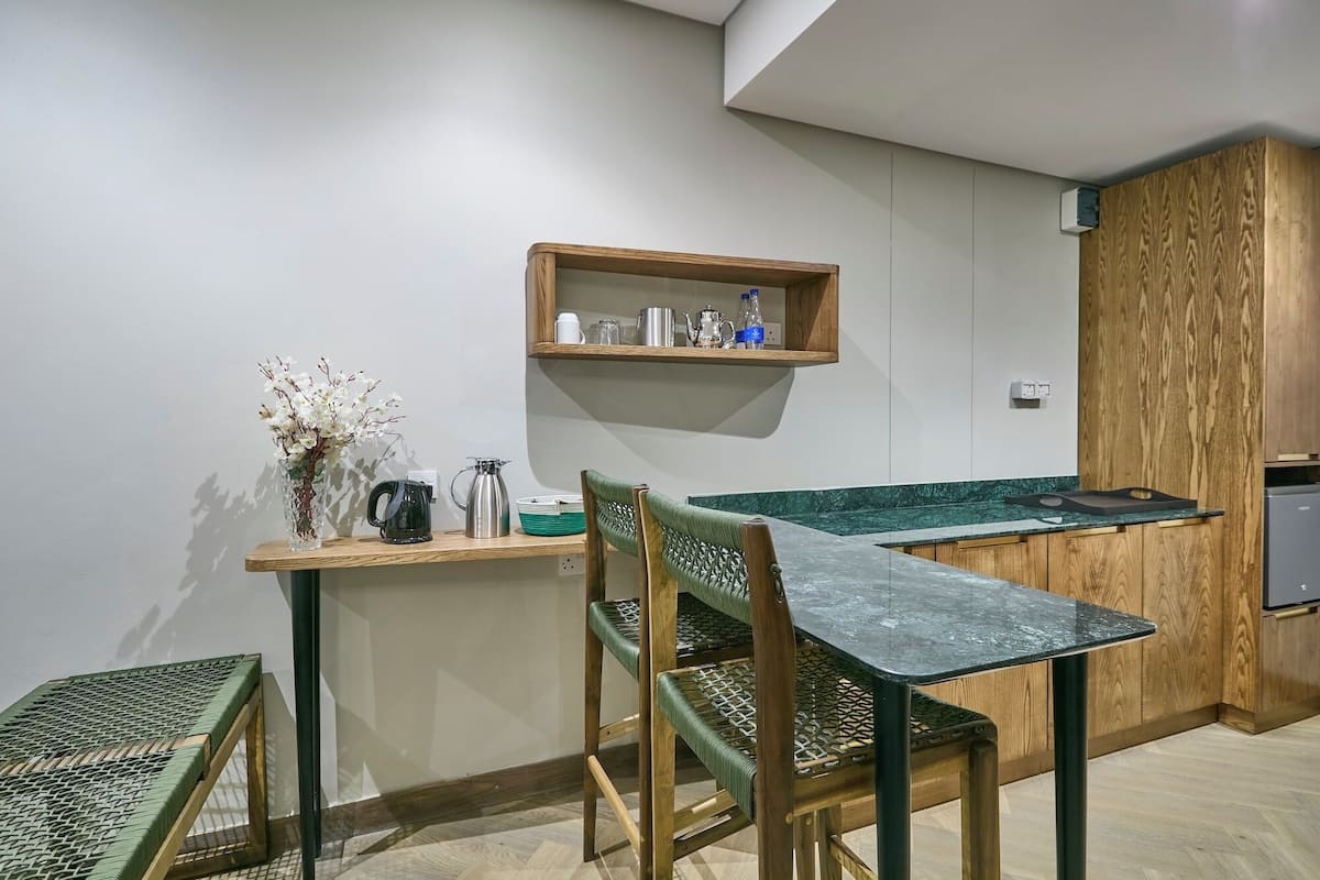Una cocina compacta con encimera de madera, un pequeño estante con utensilios de cocina y un comedor con mesa y sillas de vidrio.