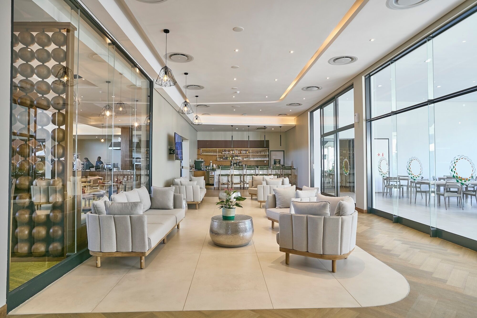 Un amplio salón con diversas opciones de asientos, un bar al fondo y grandes ventanales que ofrecen luz natural.