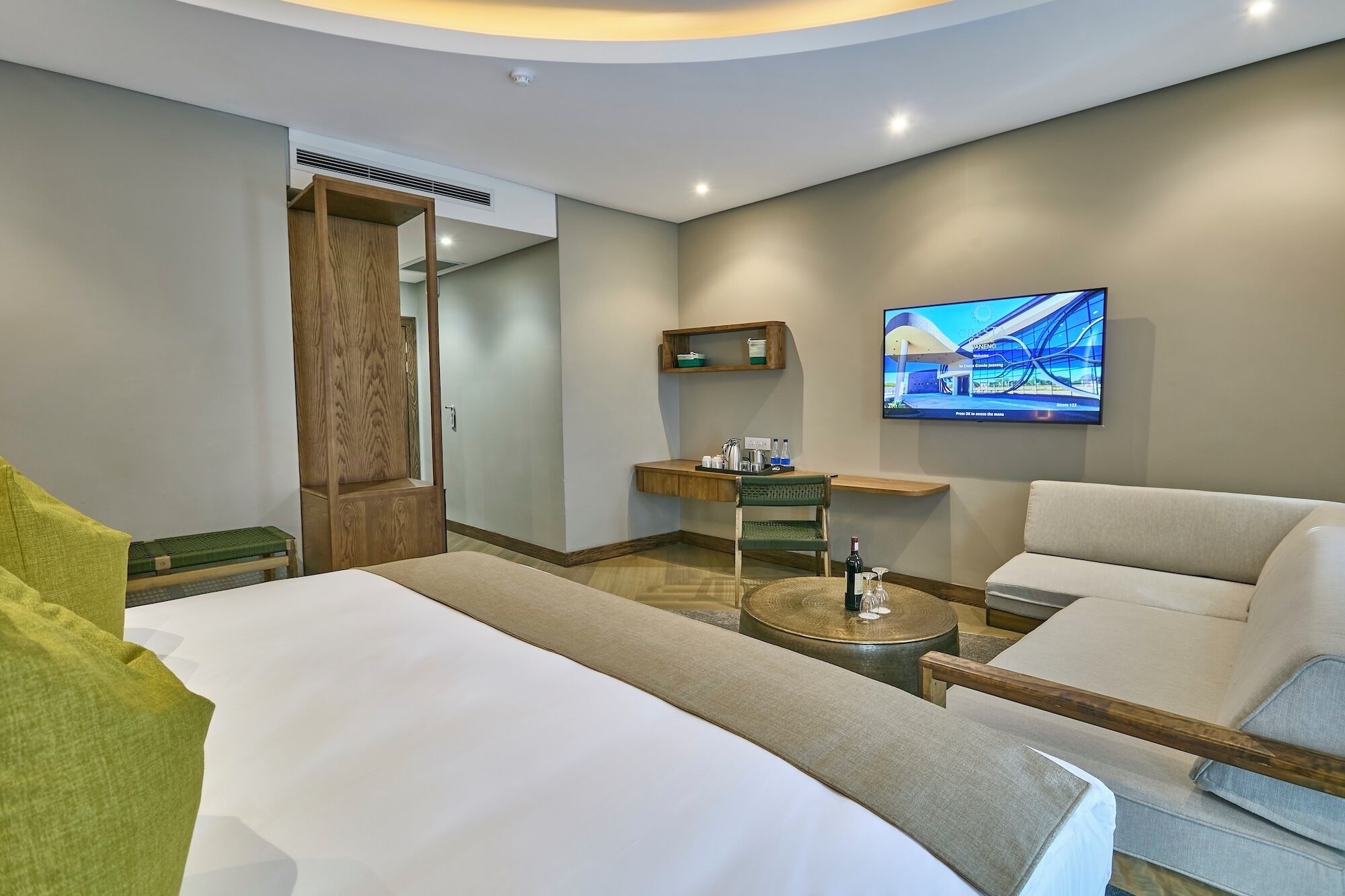 A hotel room with a bed, two armchairs, a small table, a TV, and a wooden wardrobe.