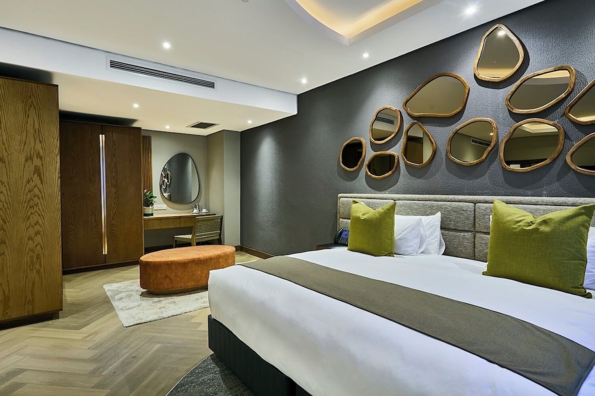 Una habitación de hotel moderna con una cama grande, un armario de madera, una tocador con espejo y una pared con varios espejos.